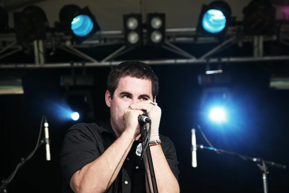 Man playing harmonica on stage with microphone and stage lights