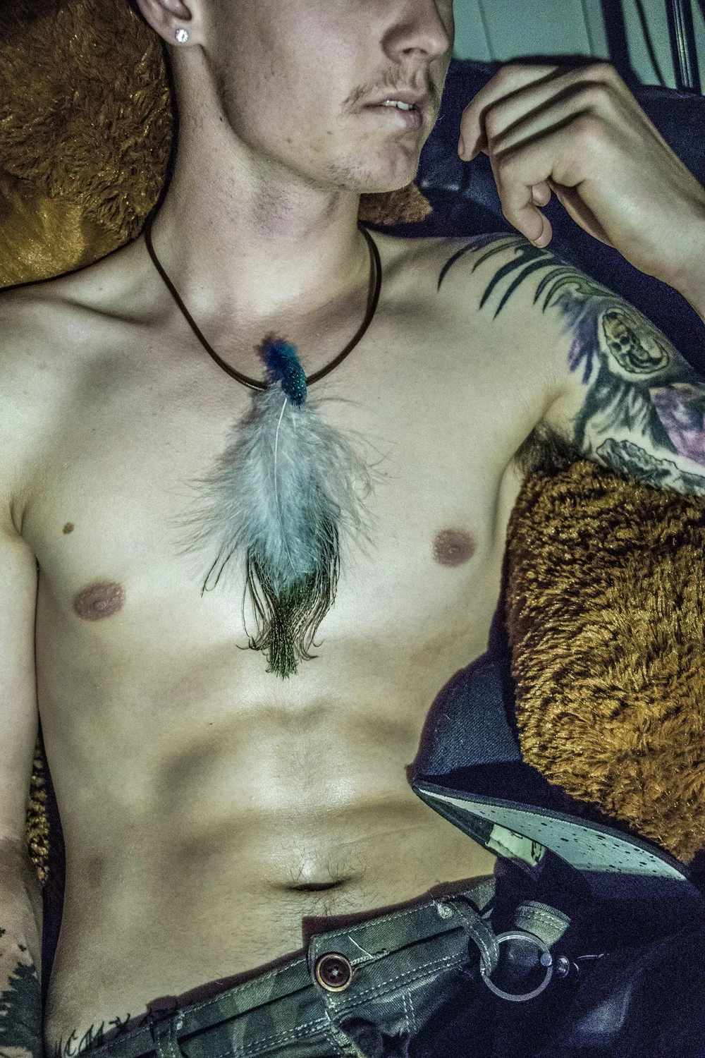 shirtless man with tattoos wearing a feather necklace