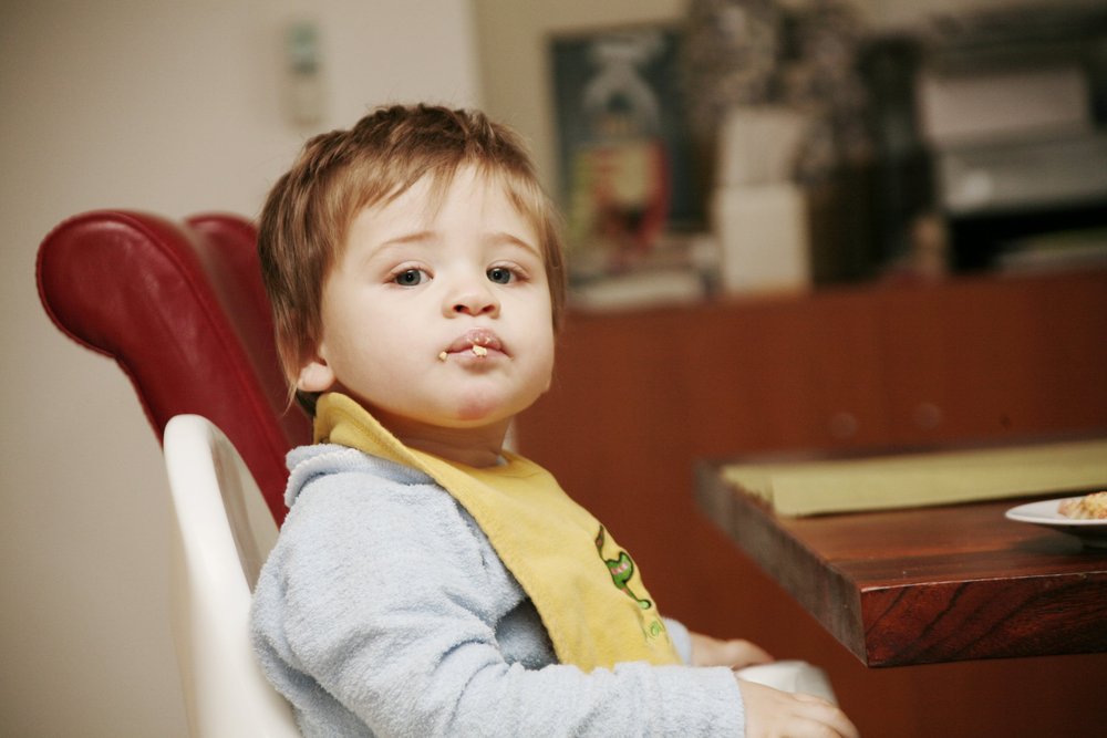 Toddler in high chair with food on face