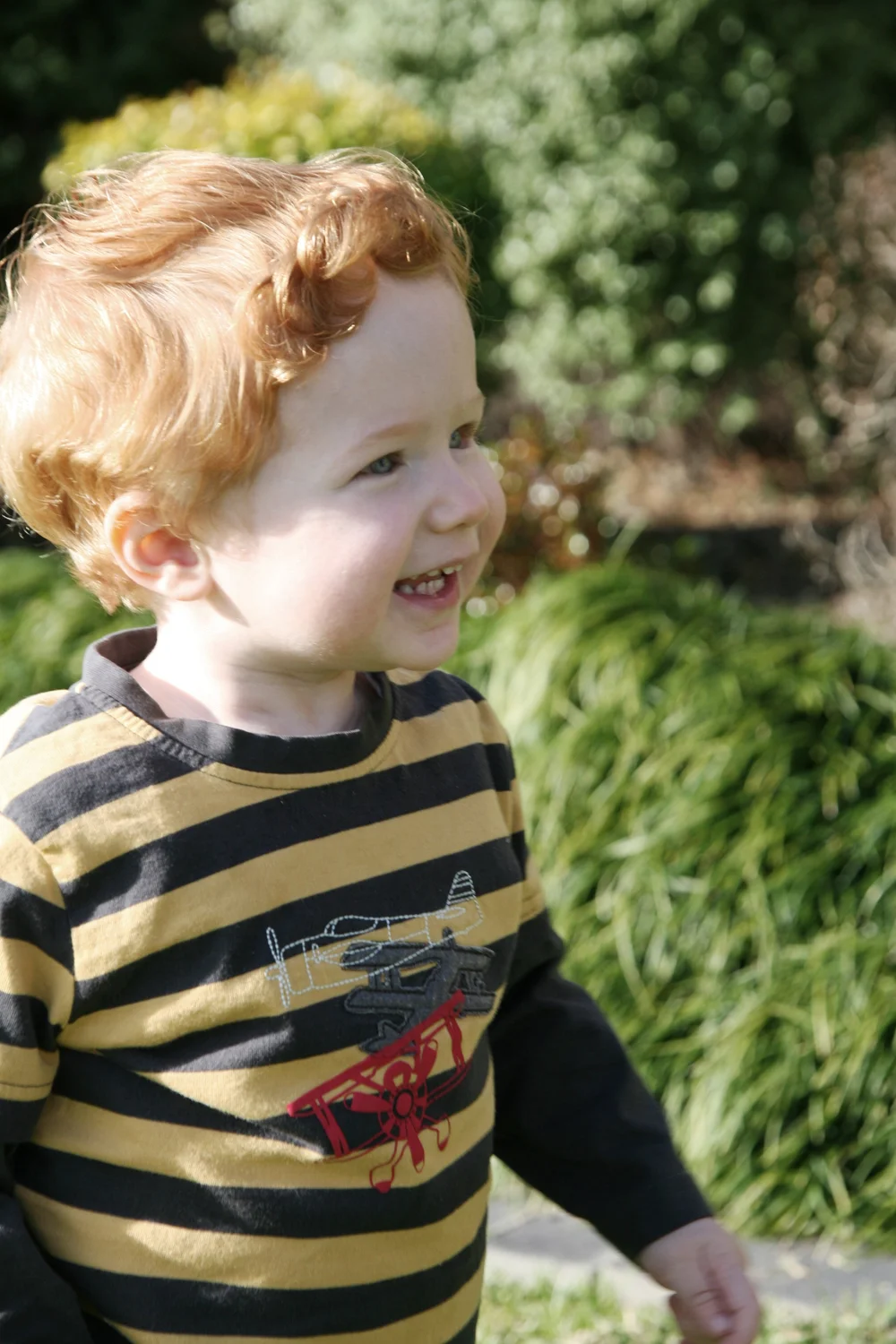 Smiling child with curly hair wearing striped sweater outdoors