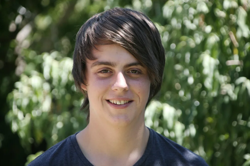Person smiling outdoors with trees in the background.