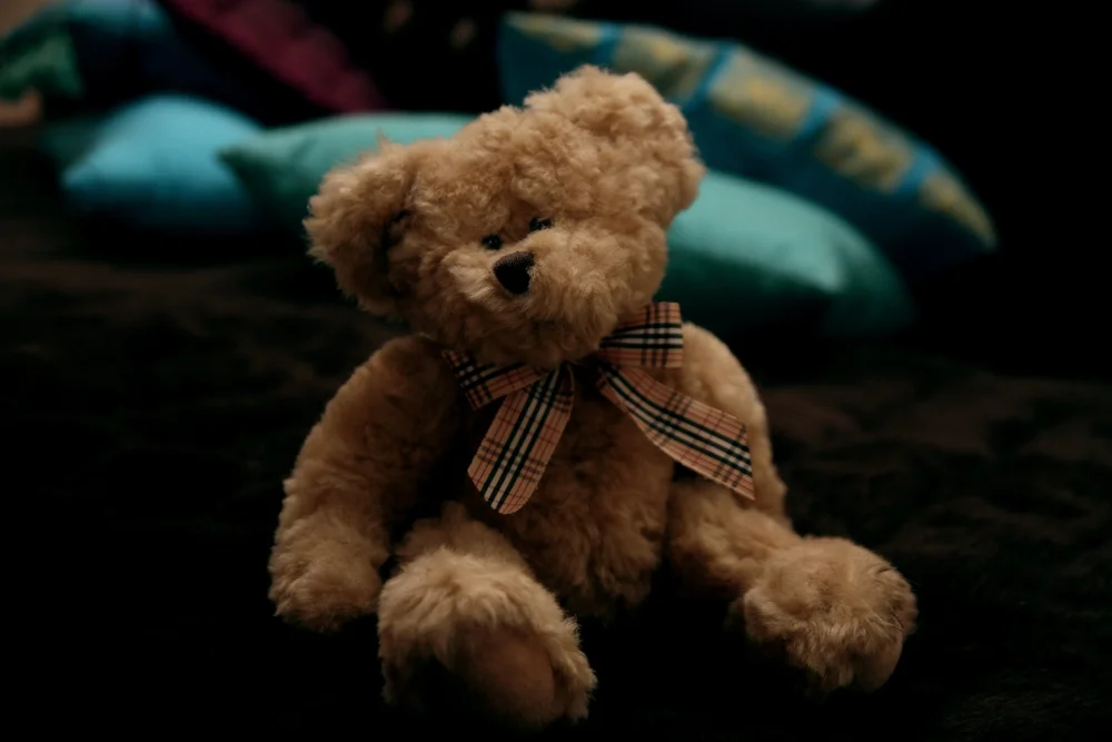 Teddy bear with plaid bowtie on bed with colorful pillows.