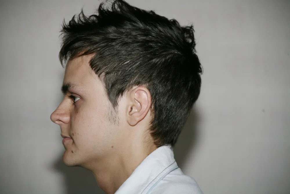 Side profile of a man with short dark hair wearing a light-colored shirt.