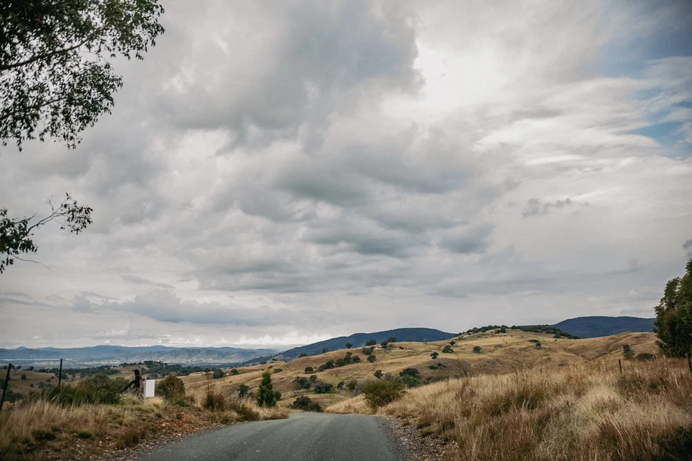 Scenic view of a rural road with grassy hills and cloudy sky