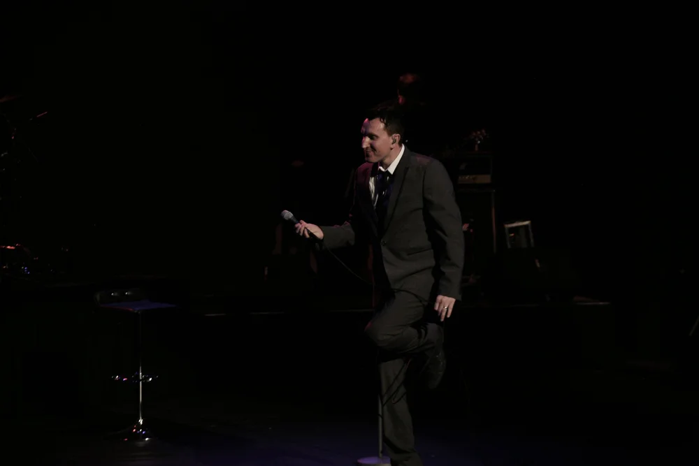 Man in suit holding microphone on dark stage