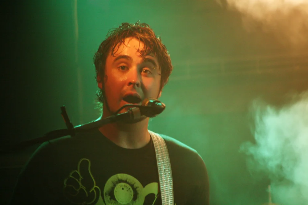 Musician singing into microphone on stage with green light and smoke effects.