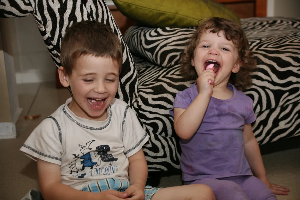 Two children laughing and playing in front of a zebra-patterned sofa.