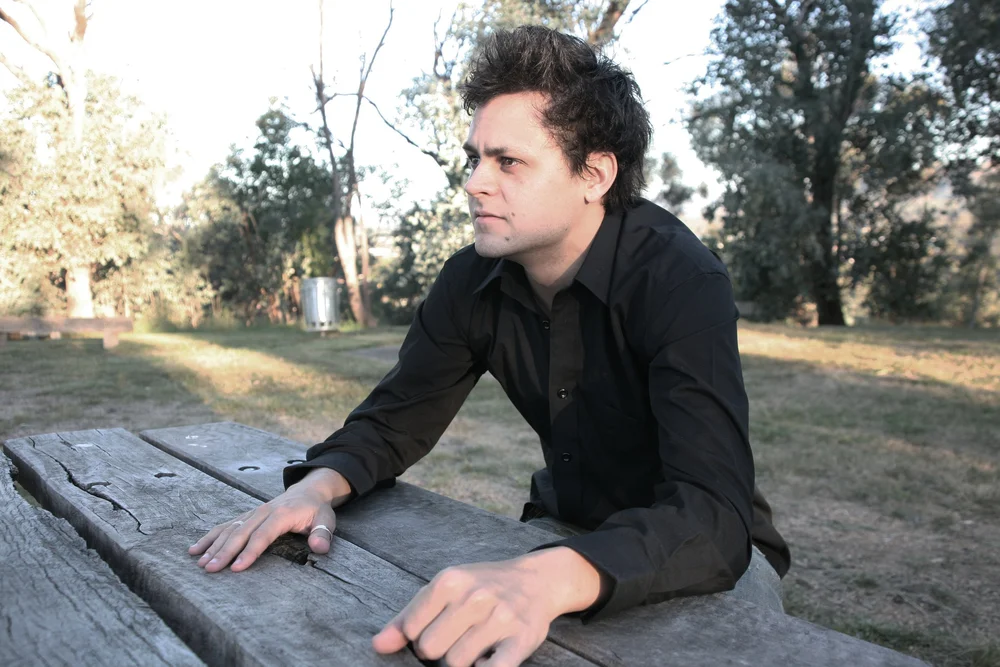 Person in black shirt sitting outdoors on a wooden bench in a park.