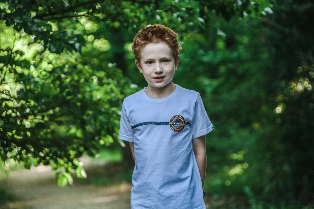 Young boy wearing a white Quiksilver t-shirt standing in a forest
