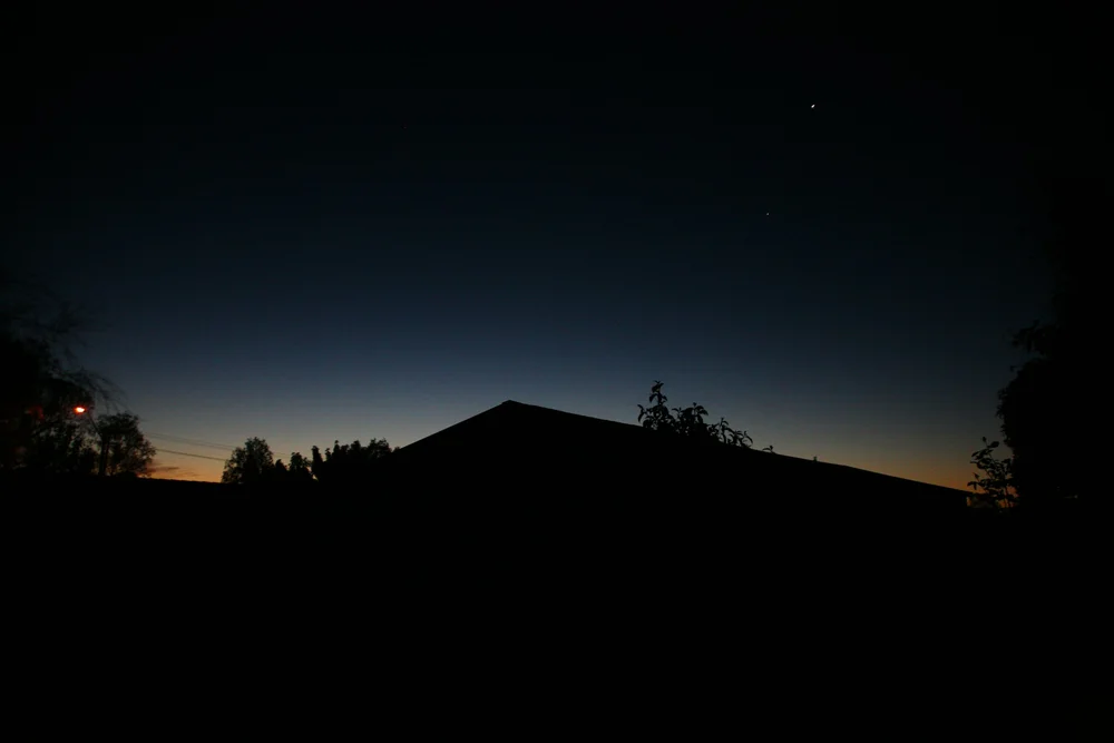 Silhouette of trees and a building during twilight with stars visible in the sky