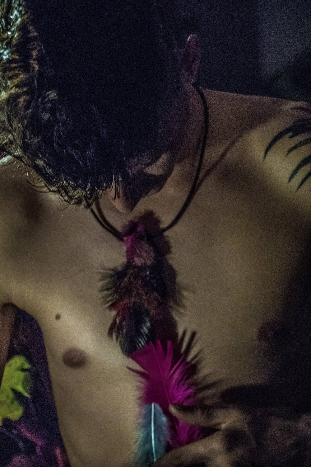 Man with a necklace of colorful feathers against a dark background