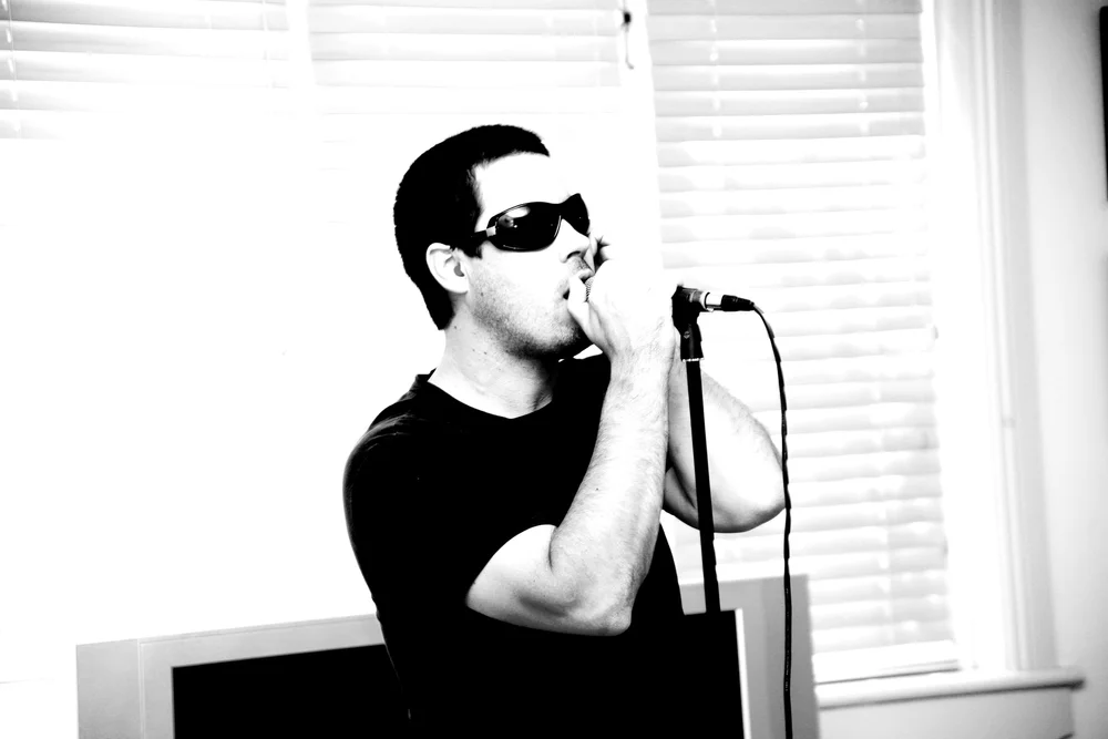 Man in sunglasses singing into a microphone indoors