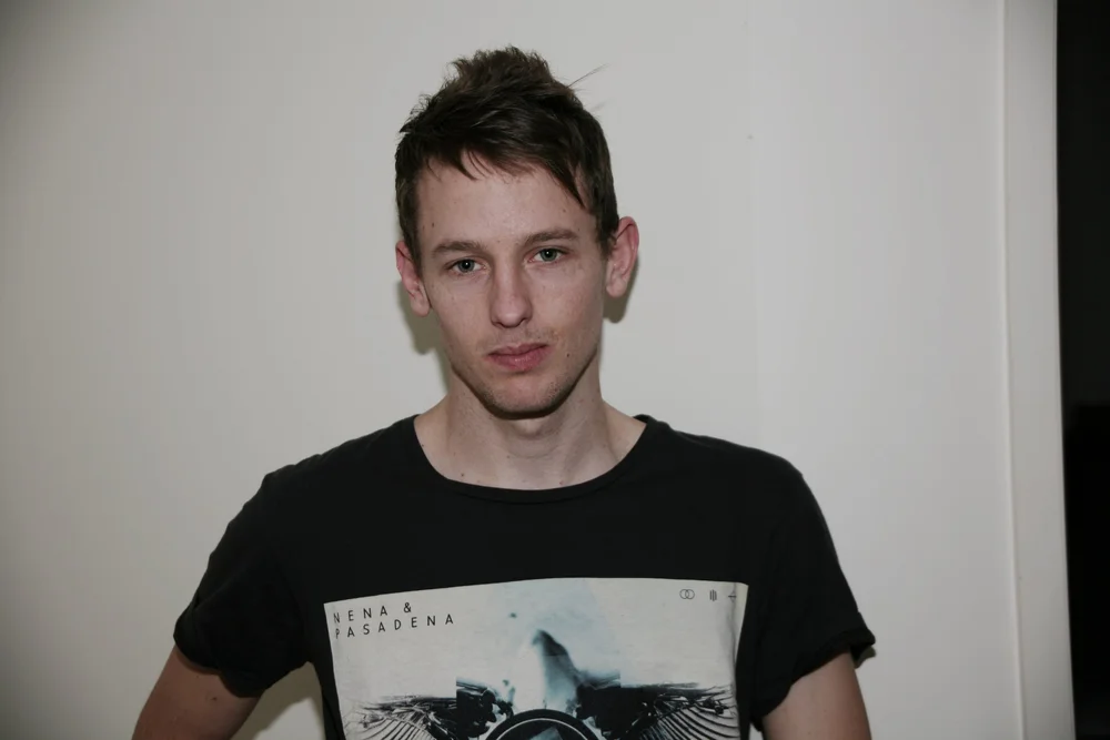 Person wearing a black T-shirt with a graphic print, standing against a plain wall.