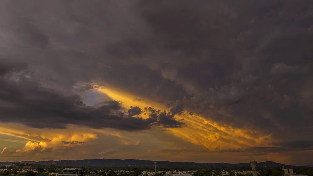Dramatic sunset with dark storm clouds and vibrant orange and yellow colors in the sky above a silhouetted landscape.