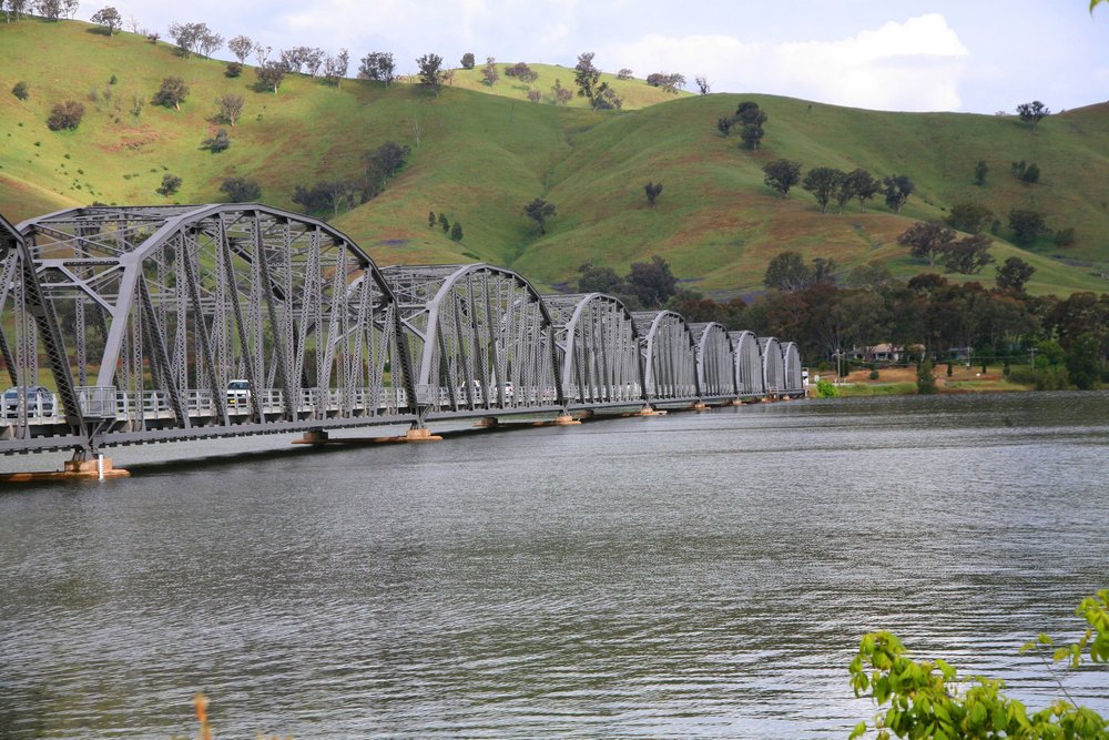 iron bridge spanning a river with rolling green hills in the background