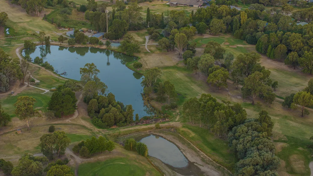 Aerial view of a golf course with lakes and green fairways, surrounded by trees and walking paths.