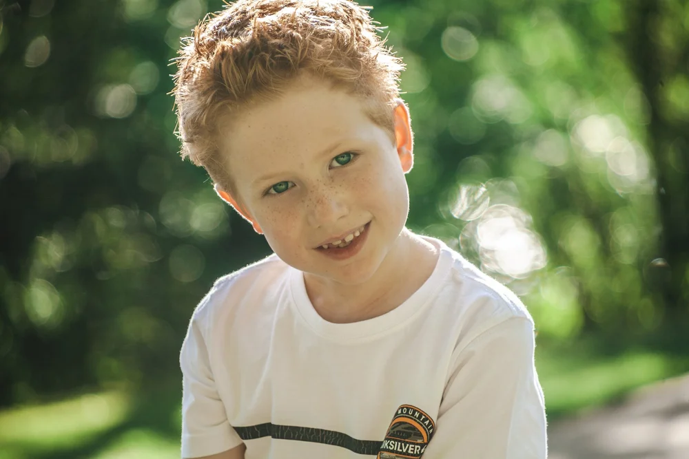 Smiling child outdoors in white shirt with blurred green background