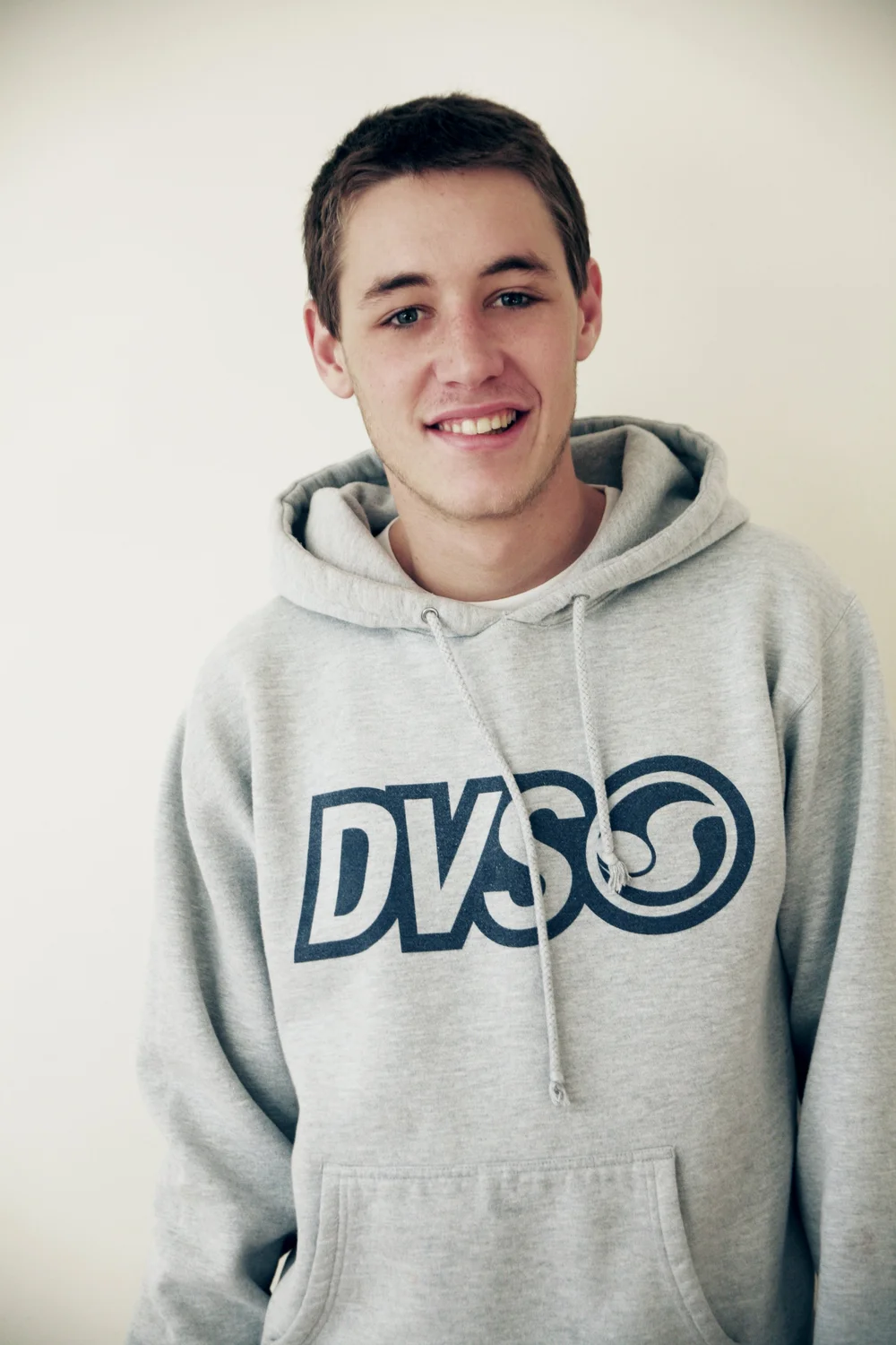 Person wearing a gray DVS logo hoodie, smiling.