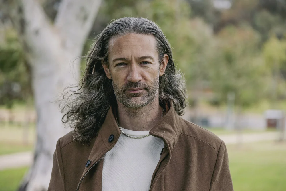 Amos outdoors in a brown jacket, with his hair loose