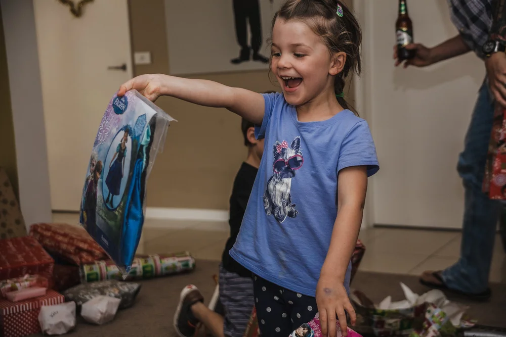 Child joyfully holding a Frozen-themed gift with wrapped presents scattered on the floor.