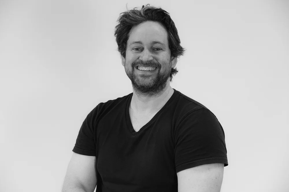 Man smiling, wearing a black shirt, against a plain background.