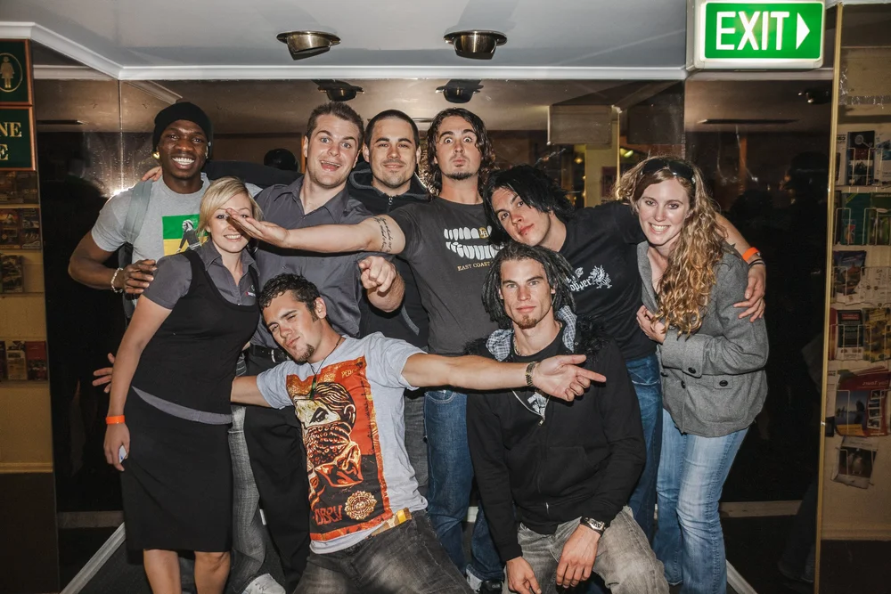 Group of smiling young adults posing indoors near an exit sign