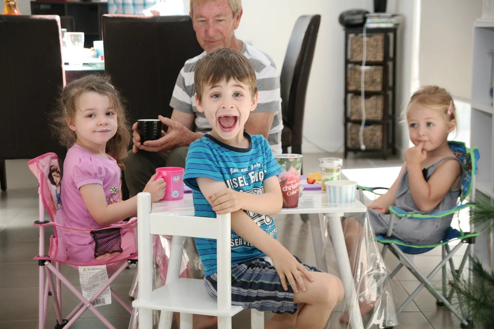 Children sitting at a small table with an older man in a home setting.