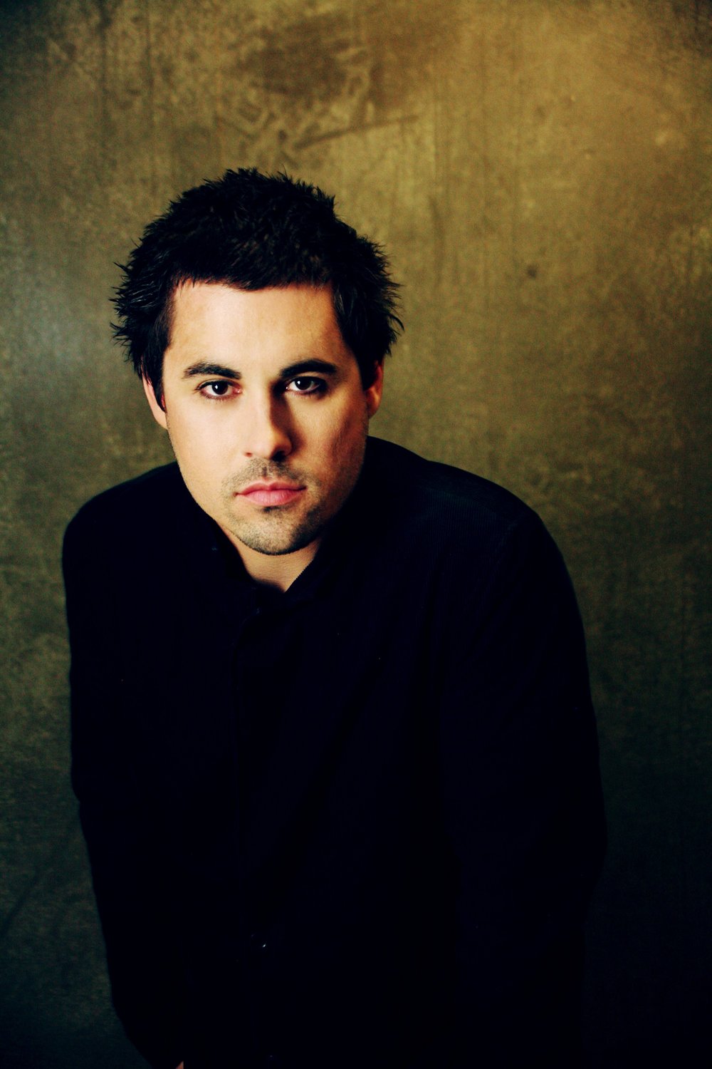 Portrait of a man with dark hair in black clothing against a textured background.