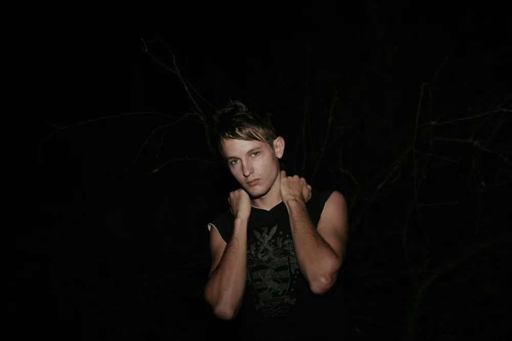 Person with short hair in dark clothing, arms crossed over chest, standing outdoors at night.
