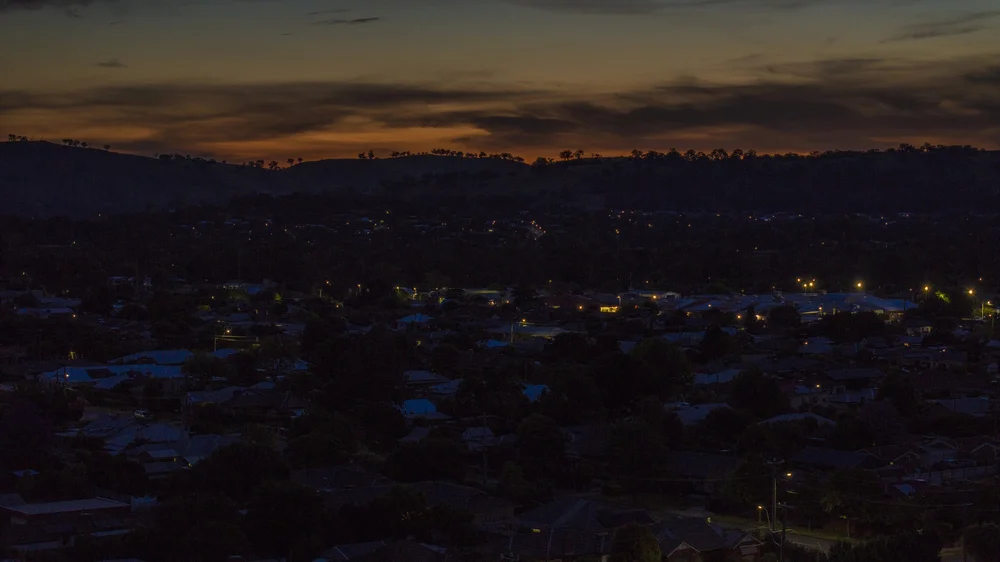 Townscape at dusk with illuminated streetlights and a silhouetted hill in the background.