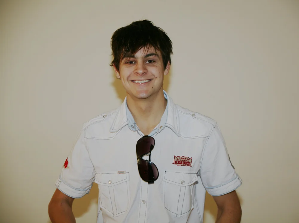 Smiling person wearing a white shirt with sunglasses hanging on it
