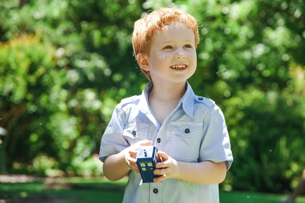 Child holding a small blue toy in a garden setting.