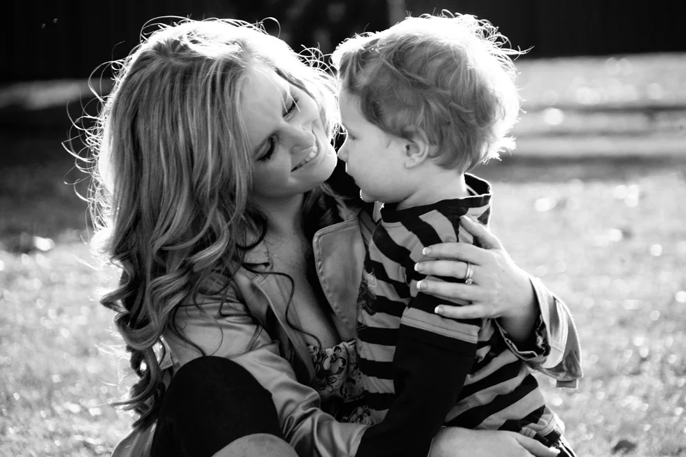 A mother and young child sharing a close moment, photographed in black and white.
