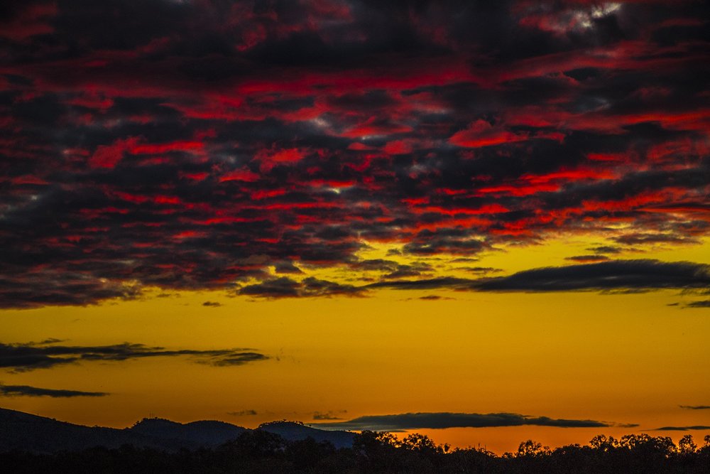 Vibrant sunset with dark clouds and red hues above a hilly landscape