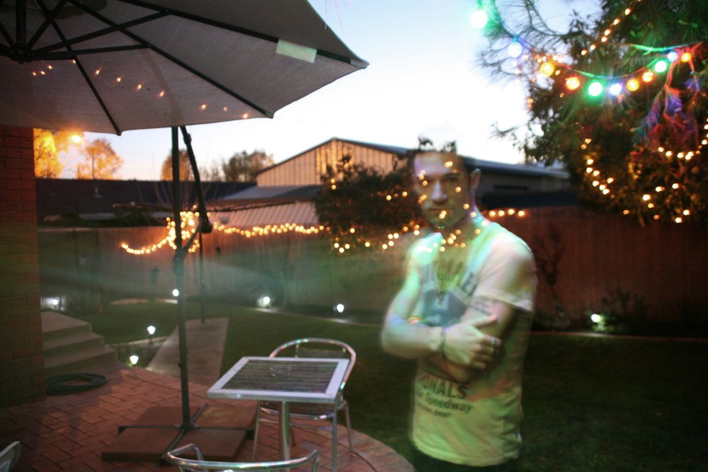 Outdoor patio with fairy lights, umbrella, table, and chair, with a blurred figure in front.