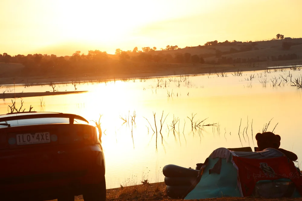 A car and camping equipment beside the weir at sunset
