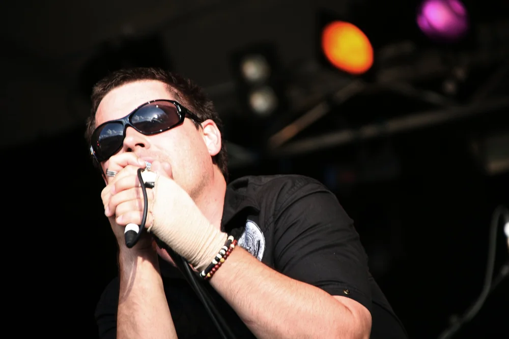Musician playing harmonica on stage with microphone and sunglasses