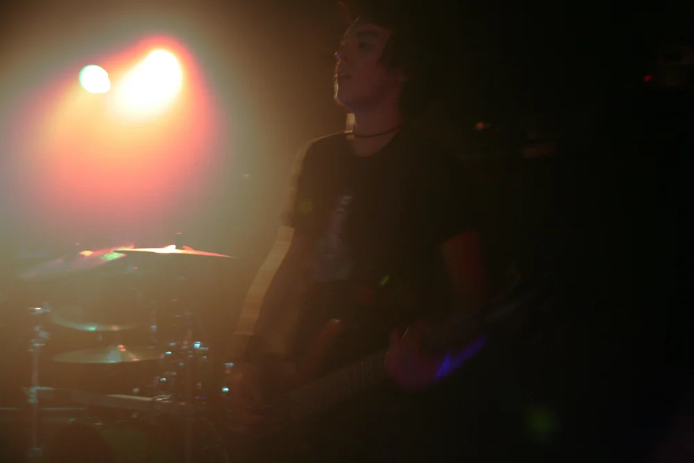 Musician on stage under red and green lights, playing guitar