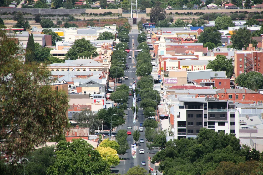 Aerial view of a city street with trees, buildings, and cars on the road.
