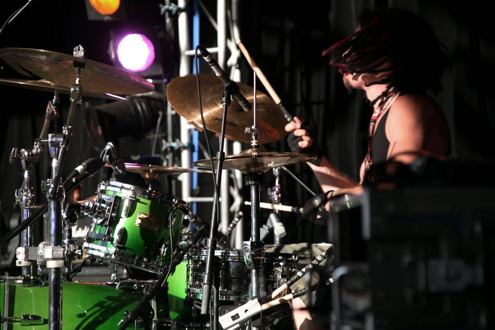 Drummer playing a green drum kit on stage with spotlights in the background