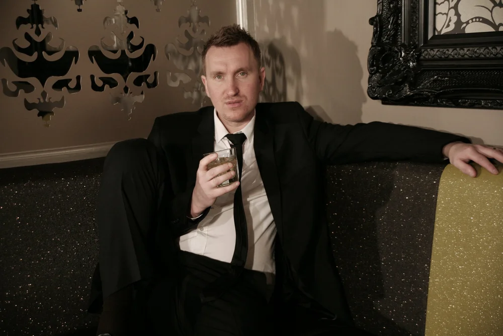 Man in suit sitting on a couch with a drink