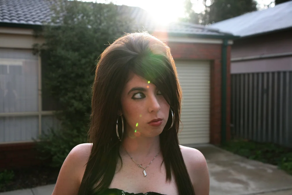 Young woman with long hair and hoop earrings standing outdoors, sunlight in background