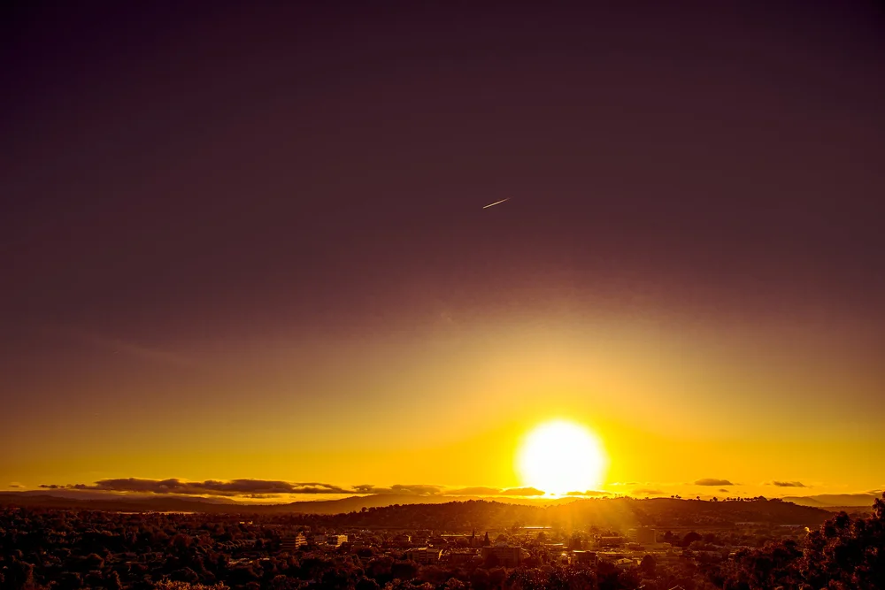 Sunset over a hilly landscape, with a vivid orange and purple sky.
