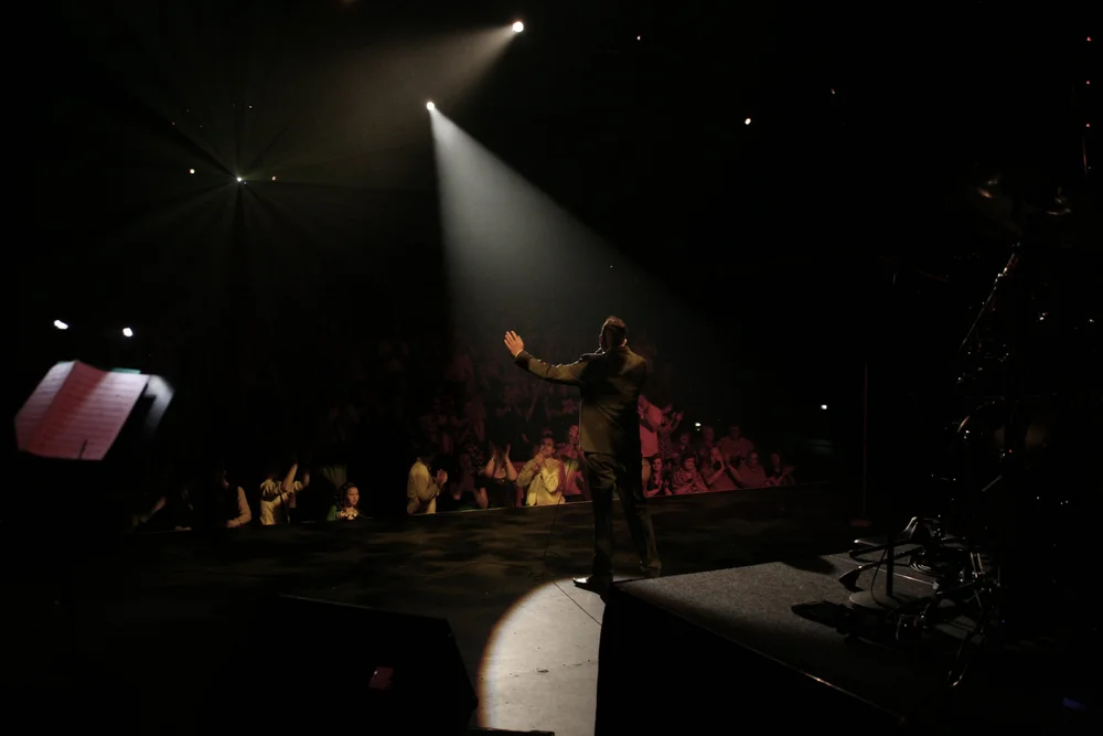 Performer on stage with microphone, facing audience, dramatic lighting