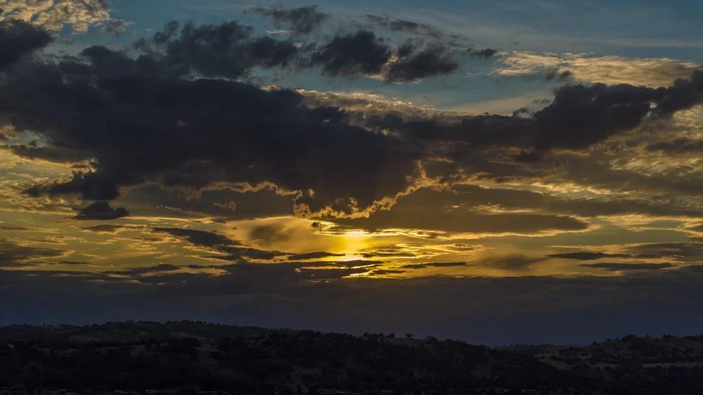 Dramatic sunset with dark clouds and golden sky over hills