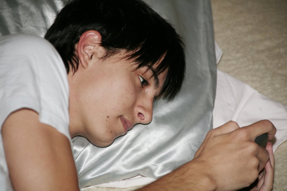 Person lying on a pillow, looking at a smartphone in hand.