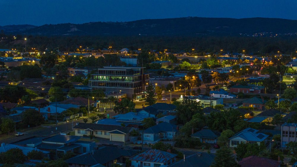 Evening cityscape with residential and commercial buildings, streetlights, and distant hills.