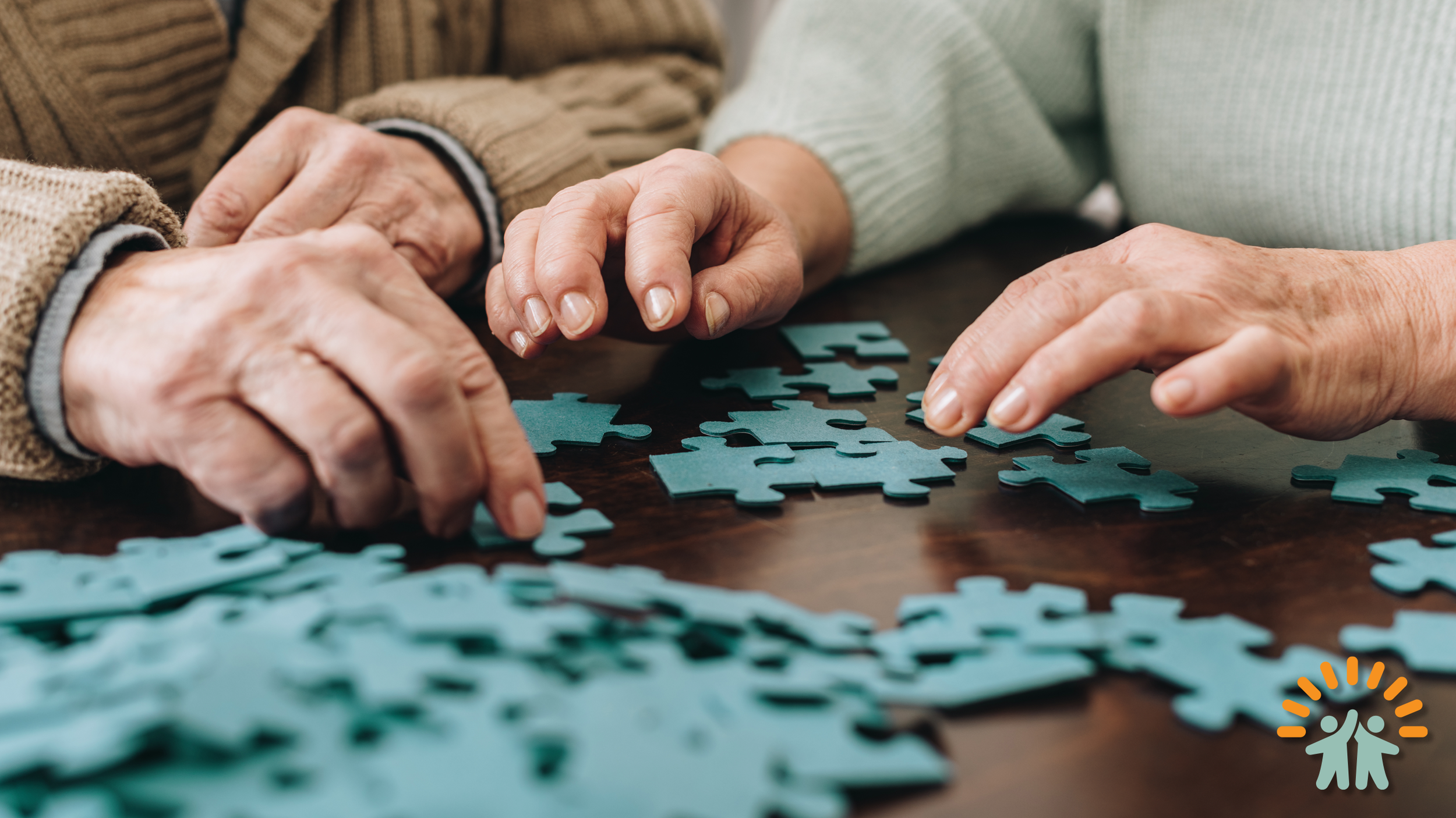 Two hands placing puzzle pieces together on a wooden table.
