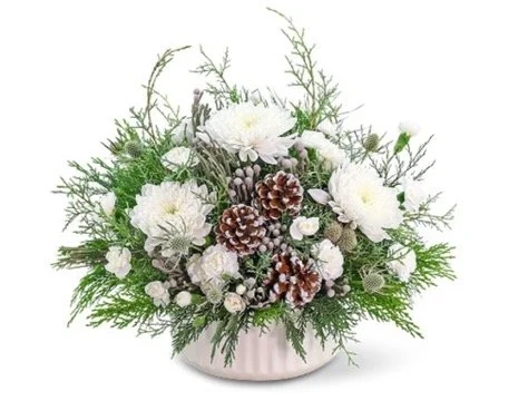 A holiday floral arrangement with white flowers, pinecones, and green foliage in a white vase.