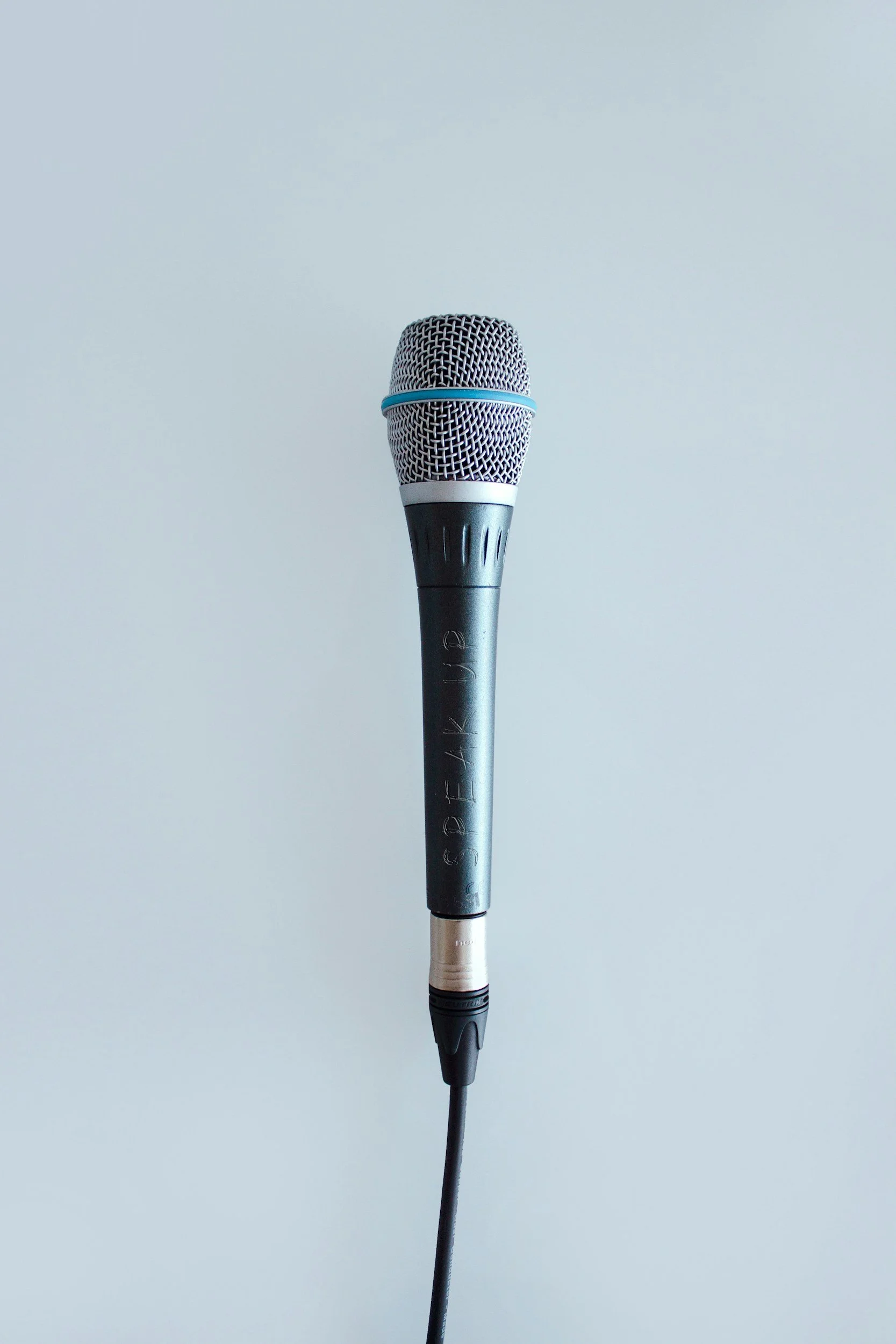 A black handheld microphone with a silver grille against a light gray background.